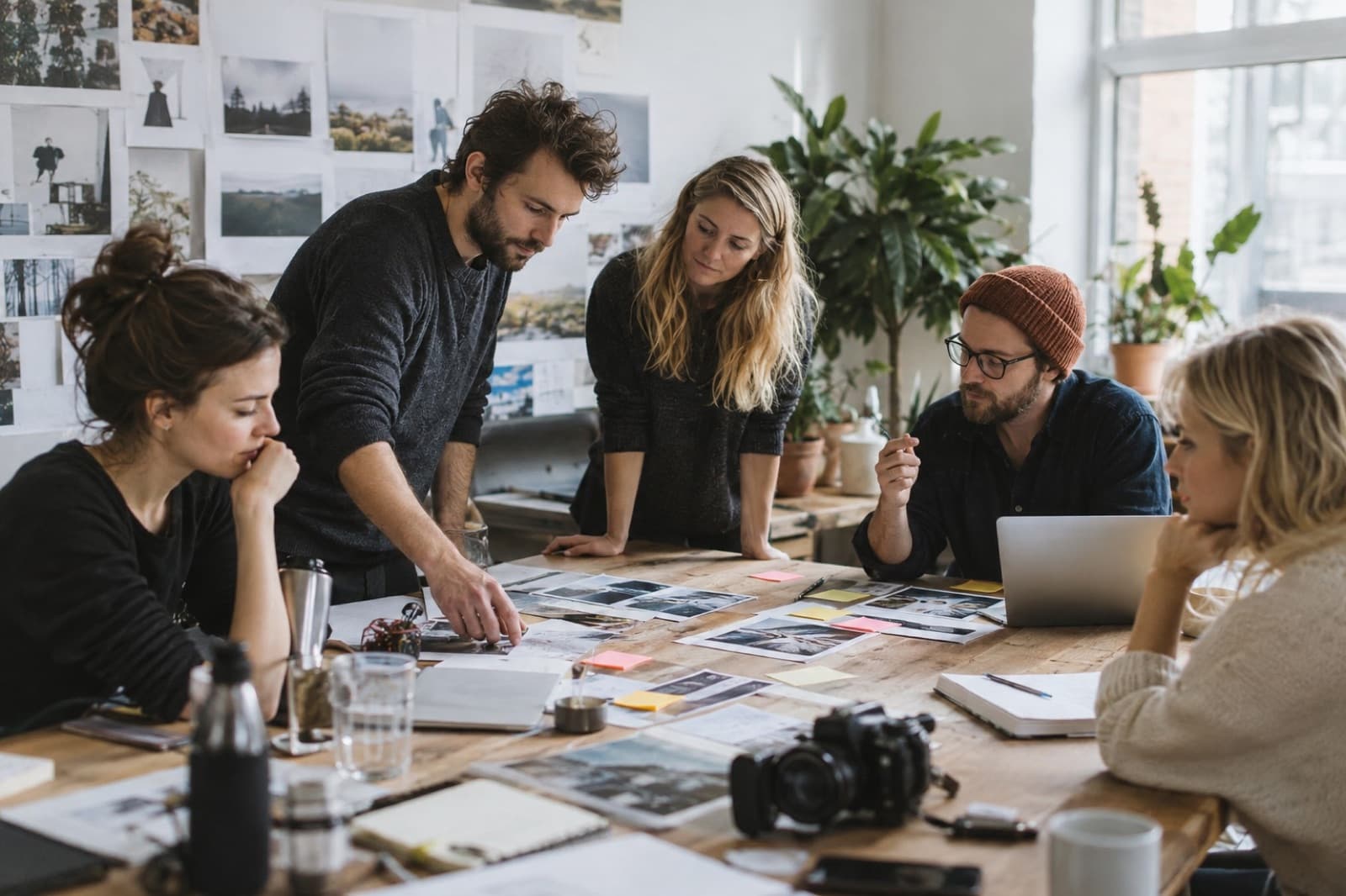 Un equipo creativo revisa fotos impresas repartidas sobre una mesa, con una cámara al lado.